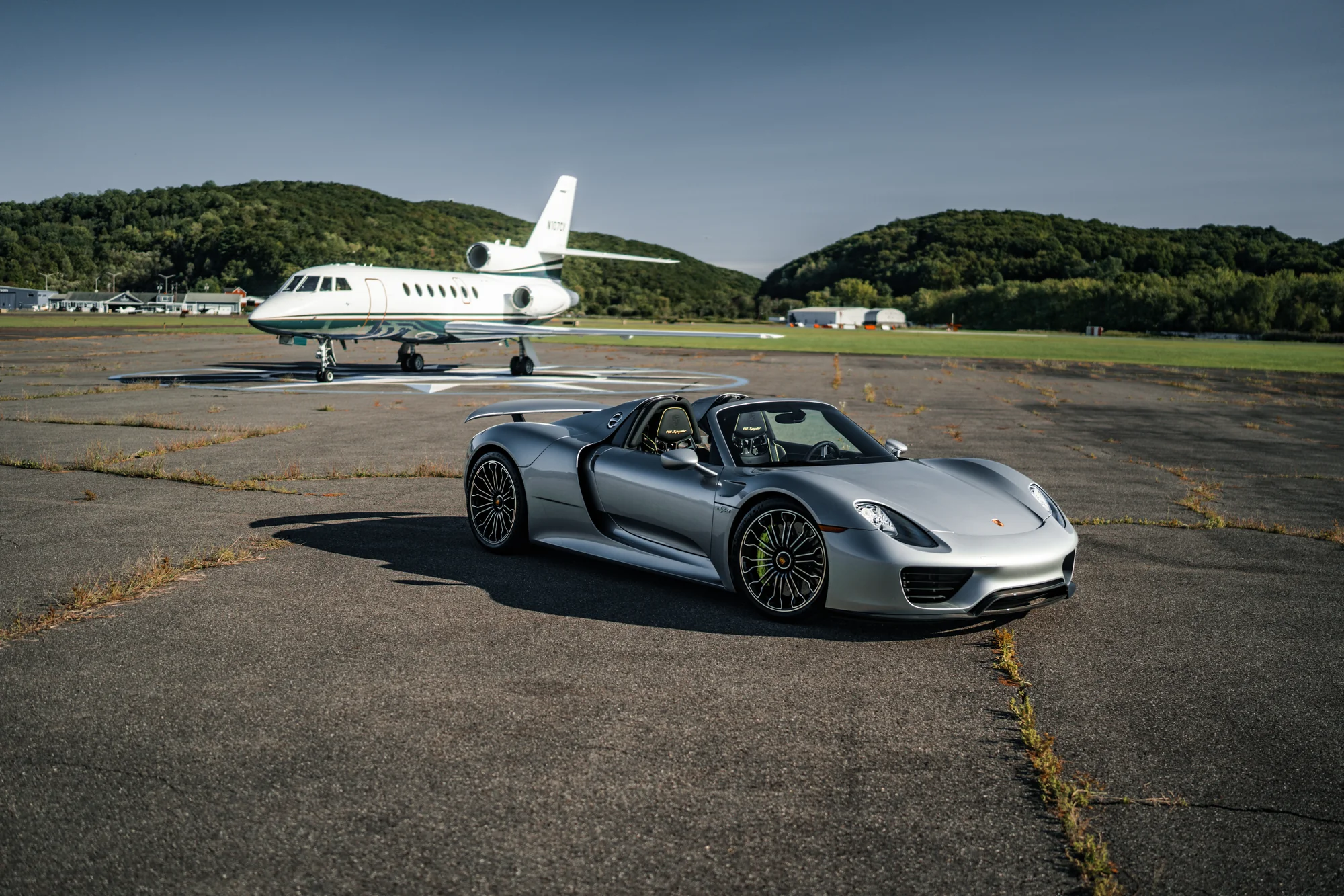 Silver Porsche 918 Spyder beside a private aircraft